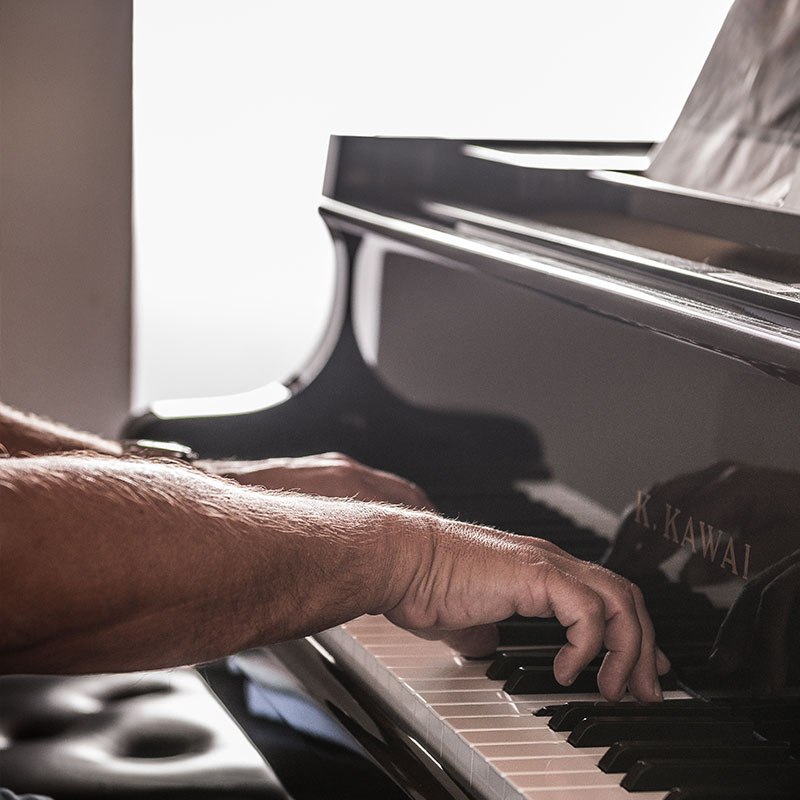 A close up of a man's hands playing the grand piano at Al Bastini